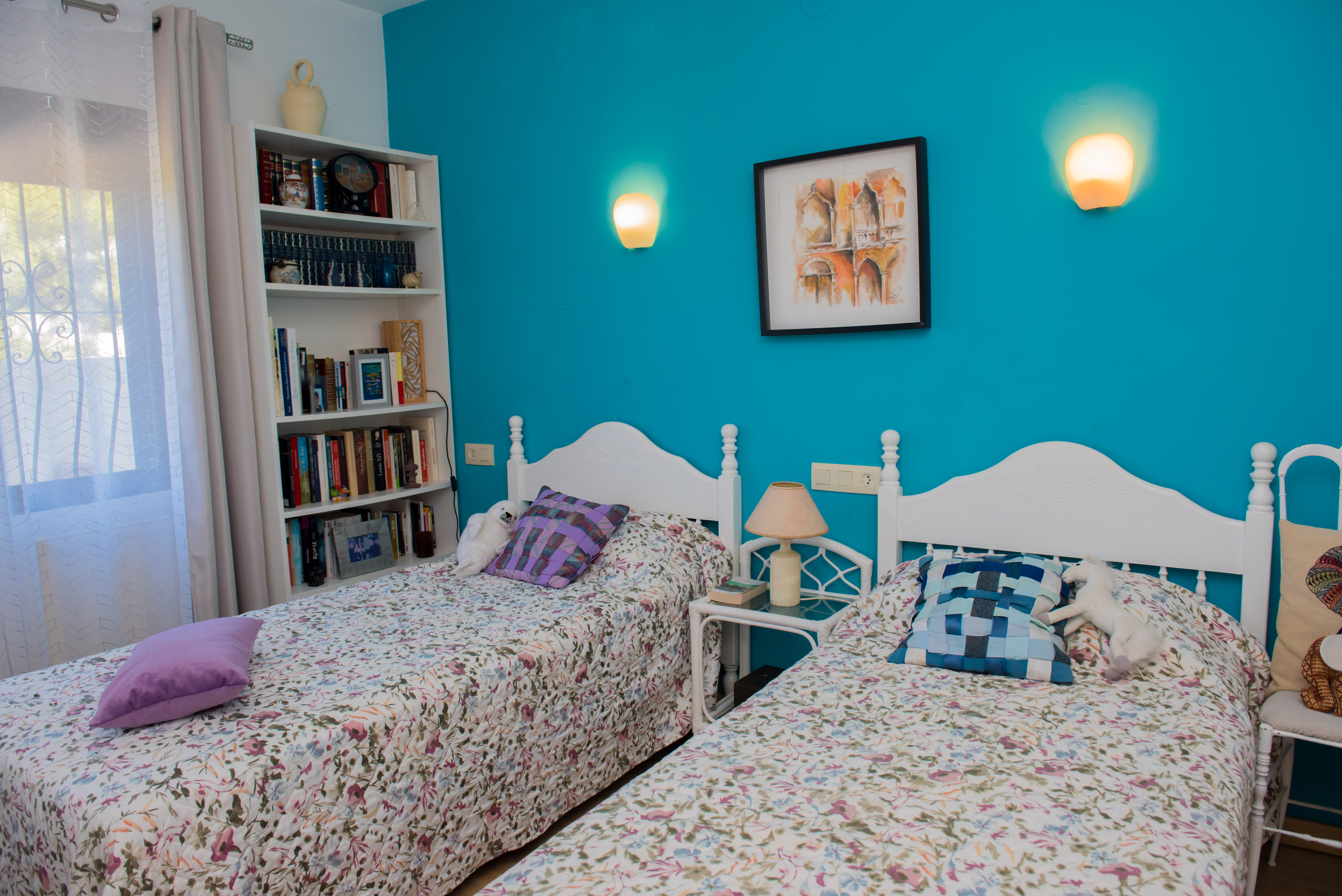 Chambre avec lits jumeaux, mur turquoise et bibliothèque blanche remplie de livres.