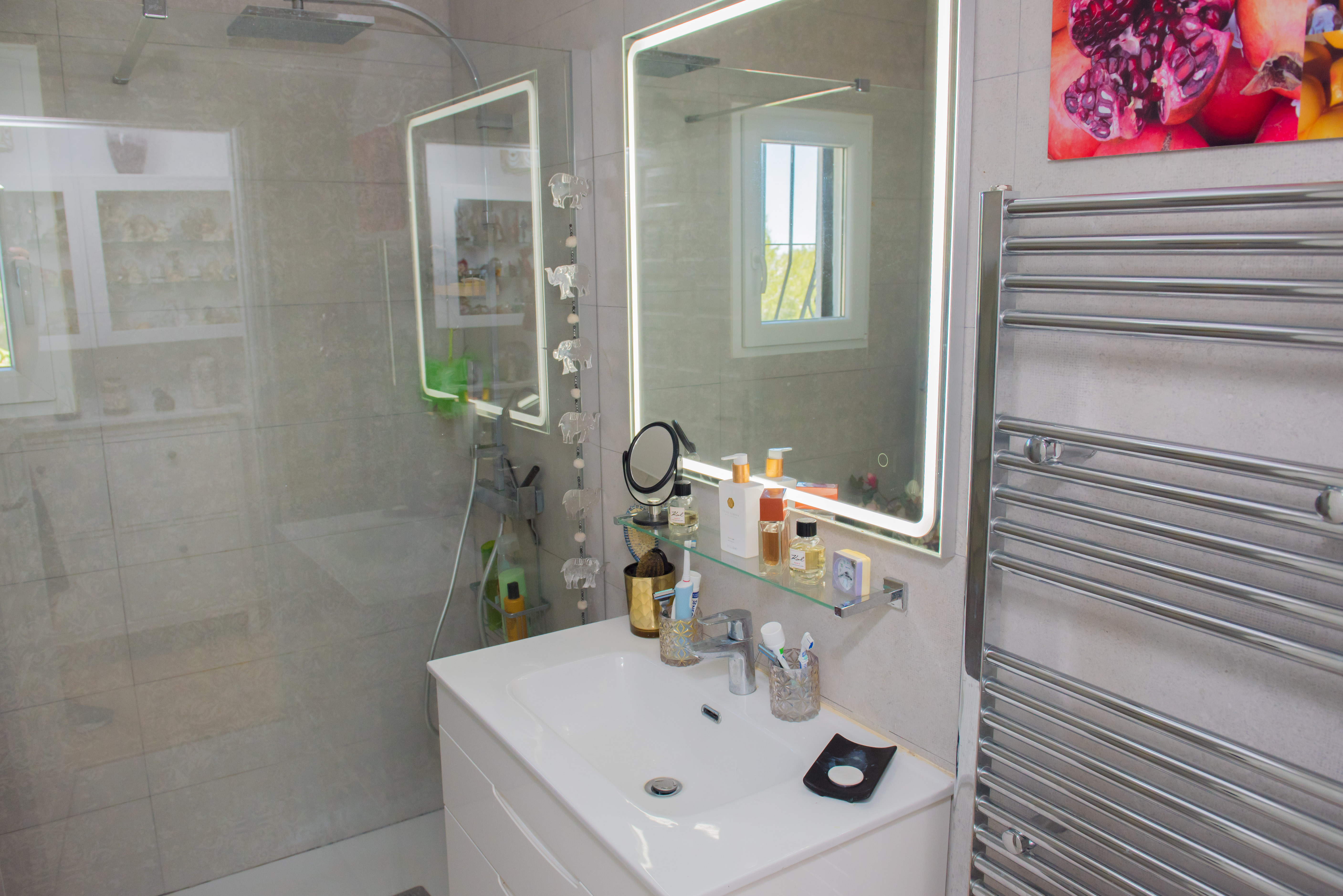Détail de la salle de bain avec lavabo blanc, miroir lumineux et sèche-serviettes chromé.