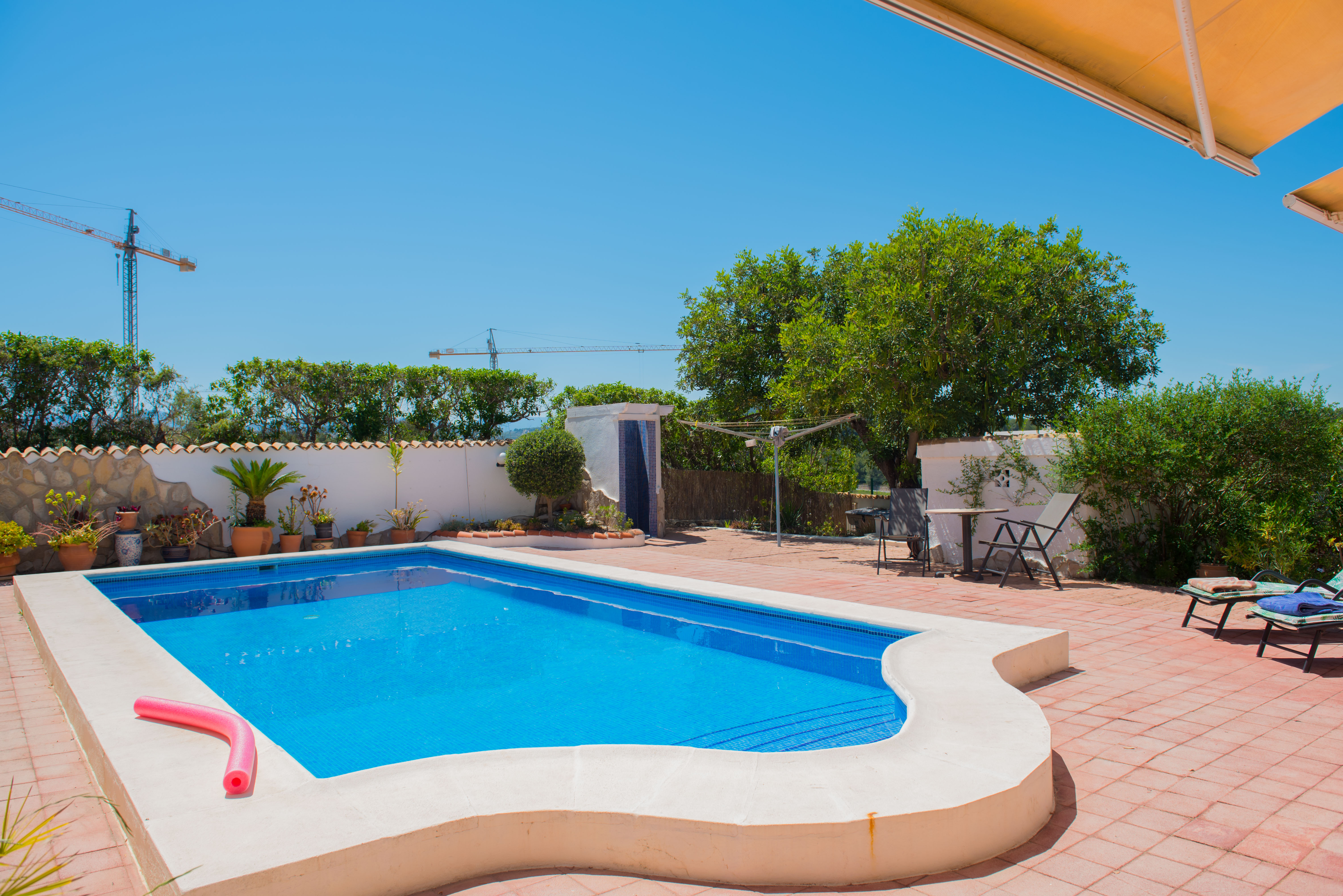 Piscine avec mosaïque bleue et bordure en ciment blanc sur patio carrelé rouge.