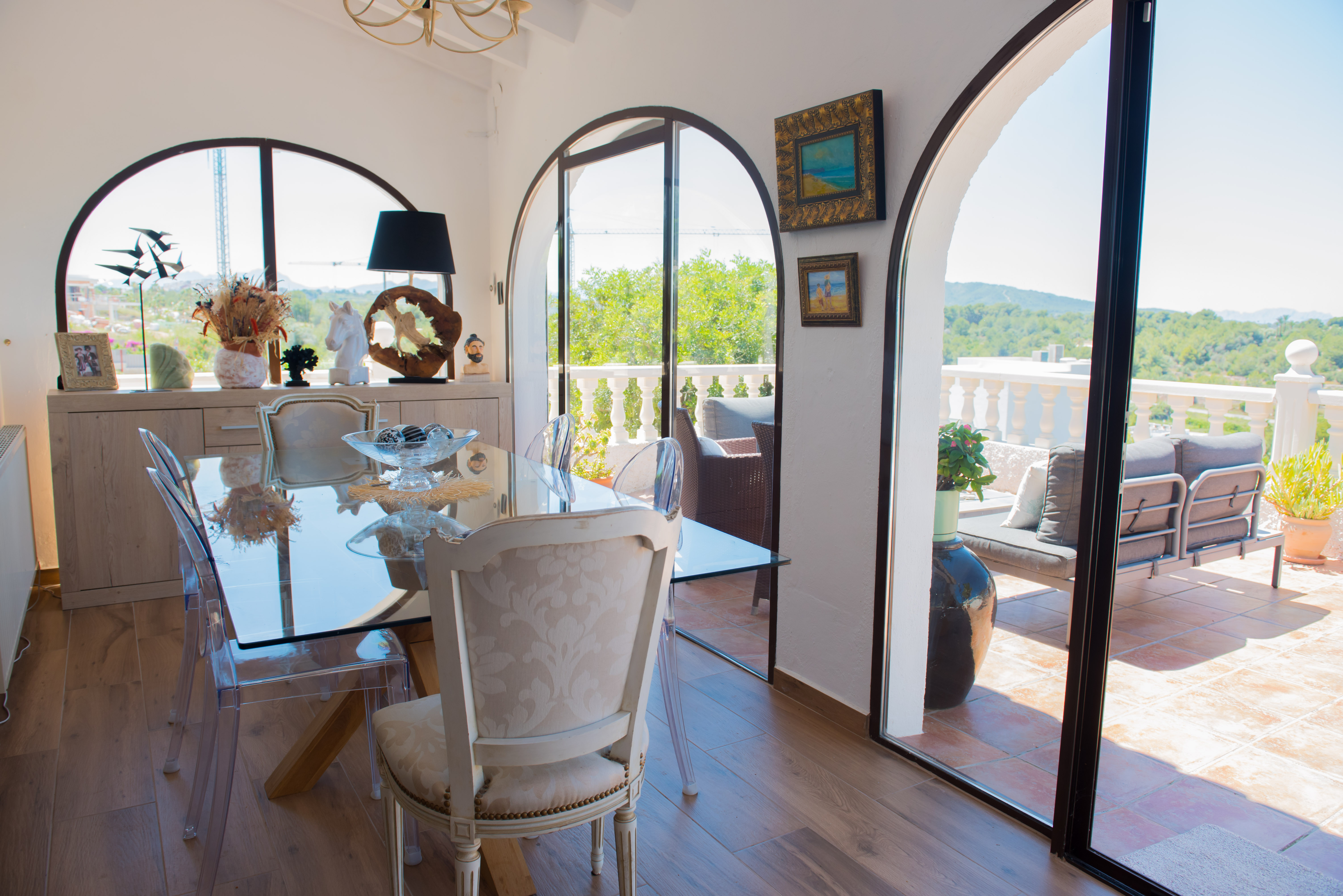 Salle à manger lumineuse avec table en verre et accès à une terrasse avec vue arborée.