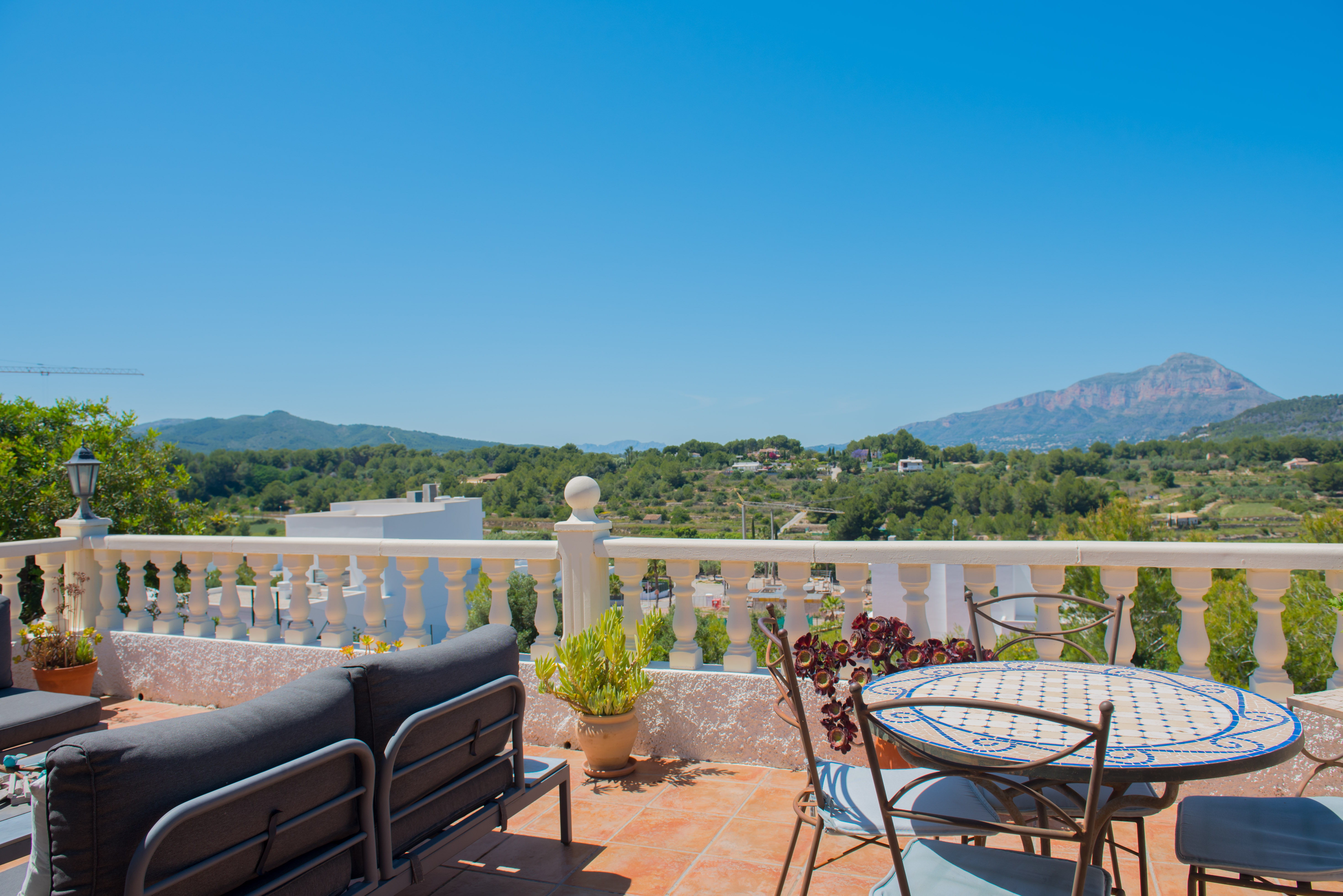 Terrasse carrelée avec vue sur la montagne, meublée d'un canapé gris et d'une table à mosaïque.