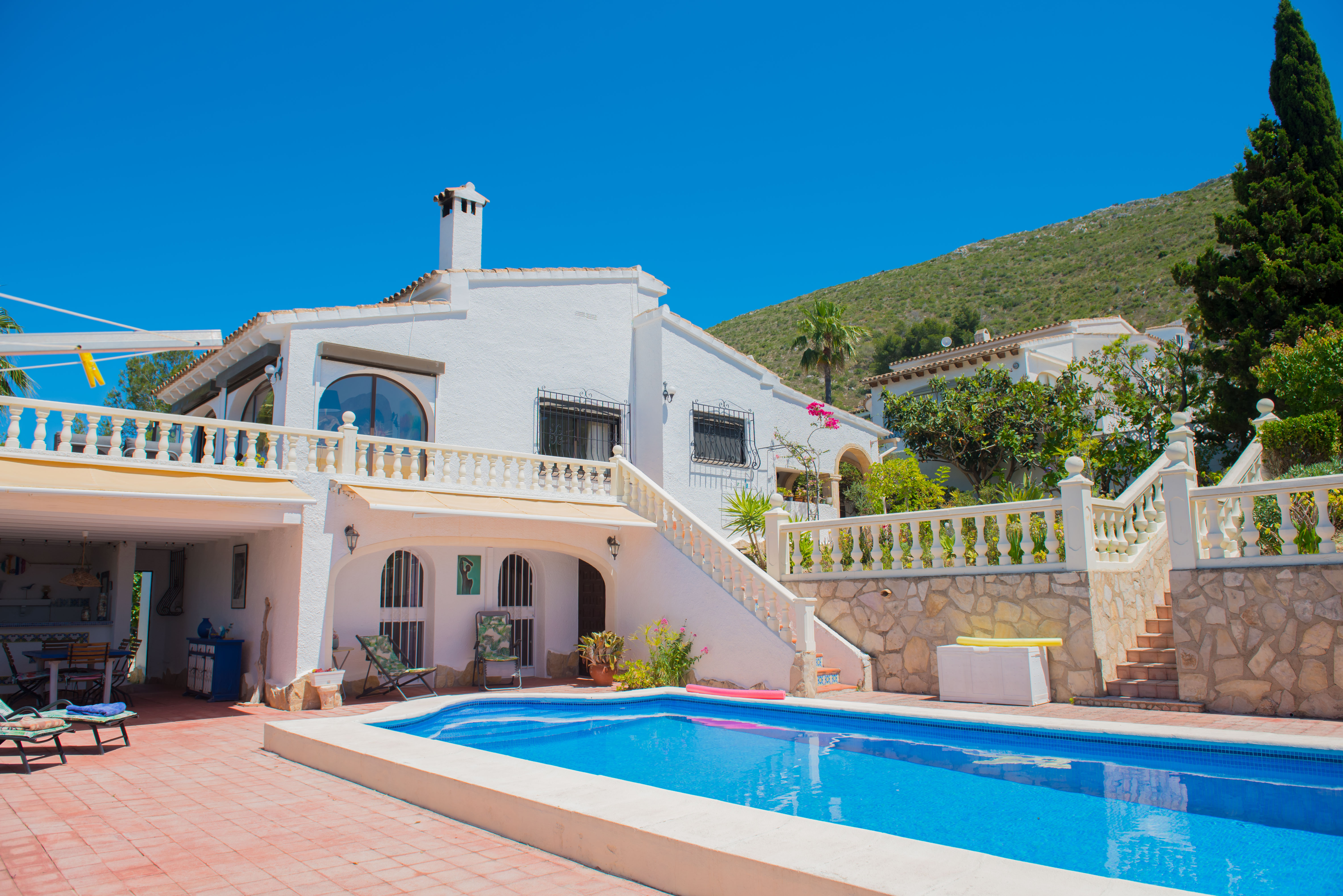 Vue sur la piscine avec carrelage rouge et maison blanche de style méditerranéen avec escalier en pierre.