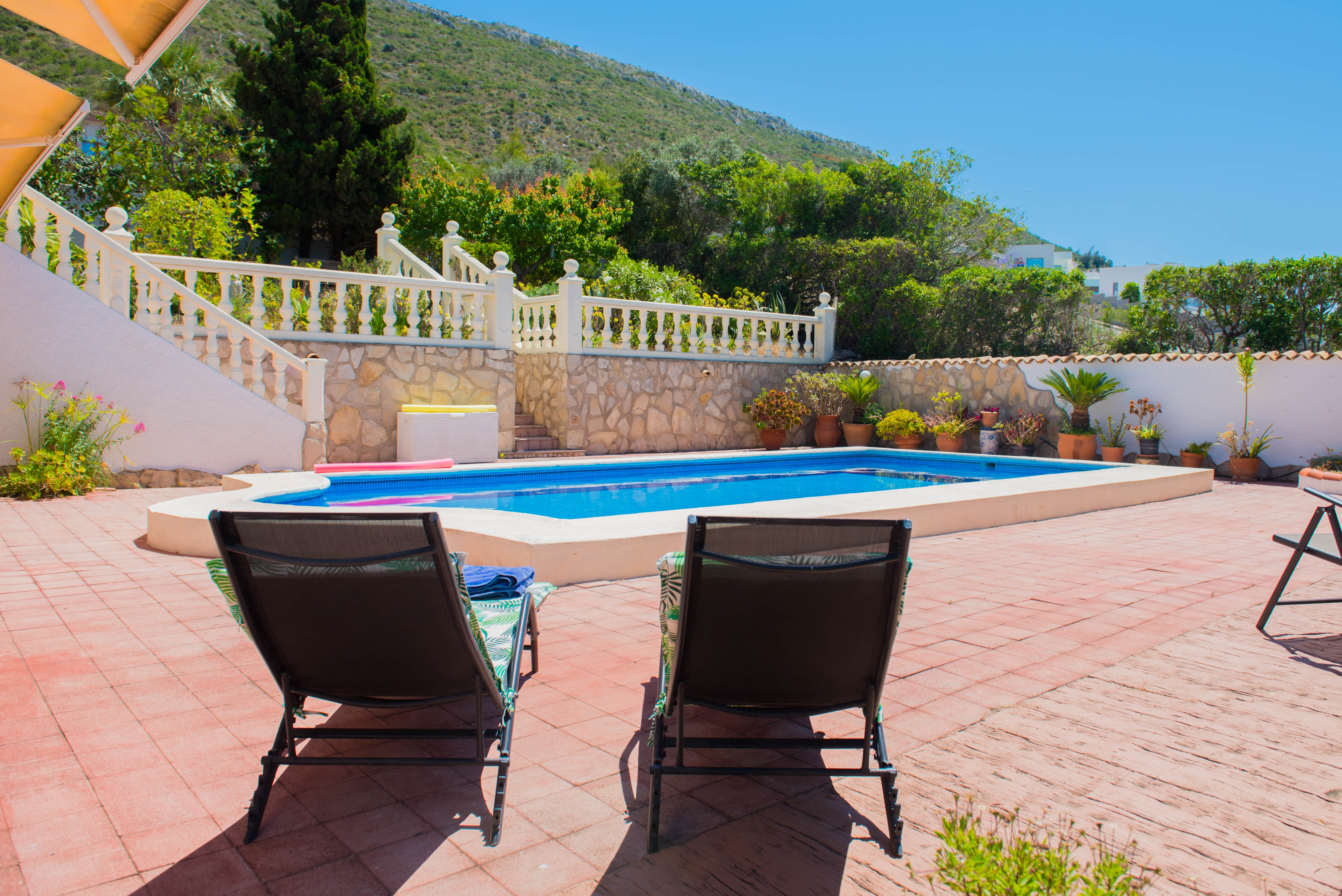 Vue sur la piscine rectangulaire carrelée de rouge avec chaises longues, entourée de verdure luxuriante.