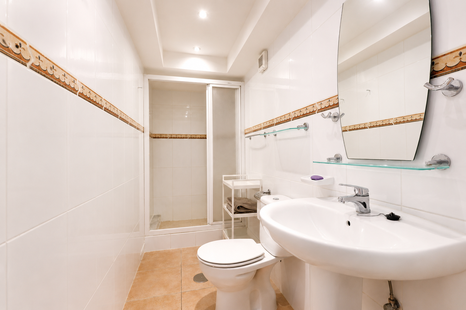 Salle de bain avec carrelage blanc, bordure décorative et sol en céramique couleur terre.