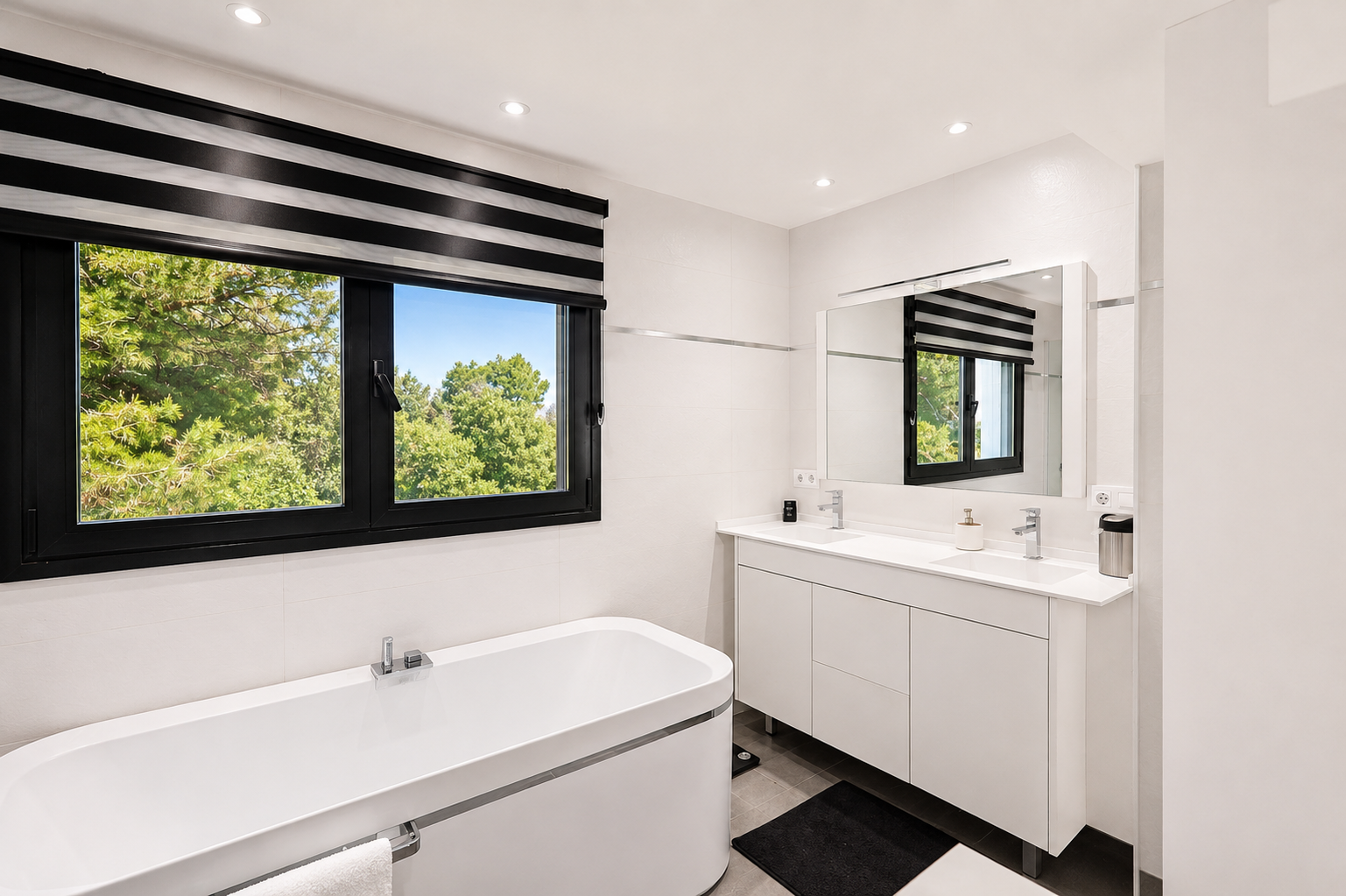 Salle de bain lumineuse avec fenêtre à cadre noir offrant une vue extérieure, baignoire blanche et meuble-lavabo double avec miroir.