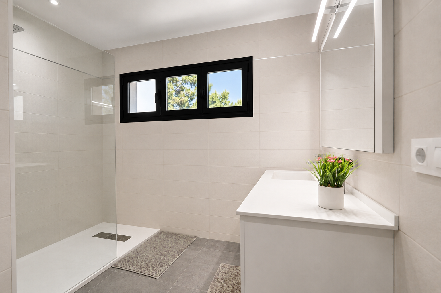 Salle de bain moderne avec douche vitrée, meuble-lavabo blanc et fenêtre à cadre noir apportant de la lumière naturelle.