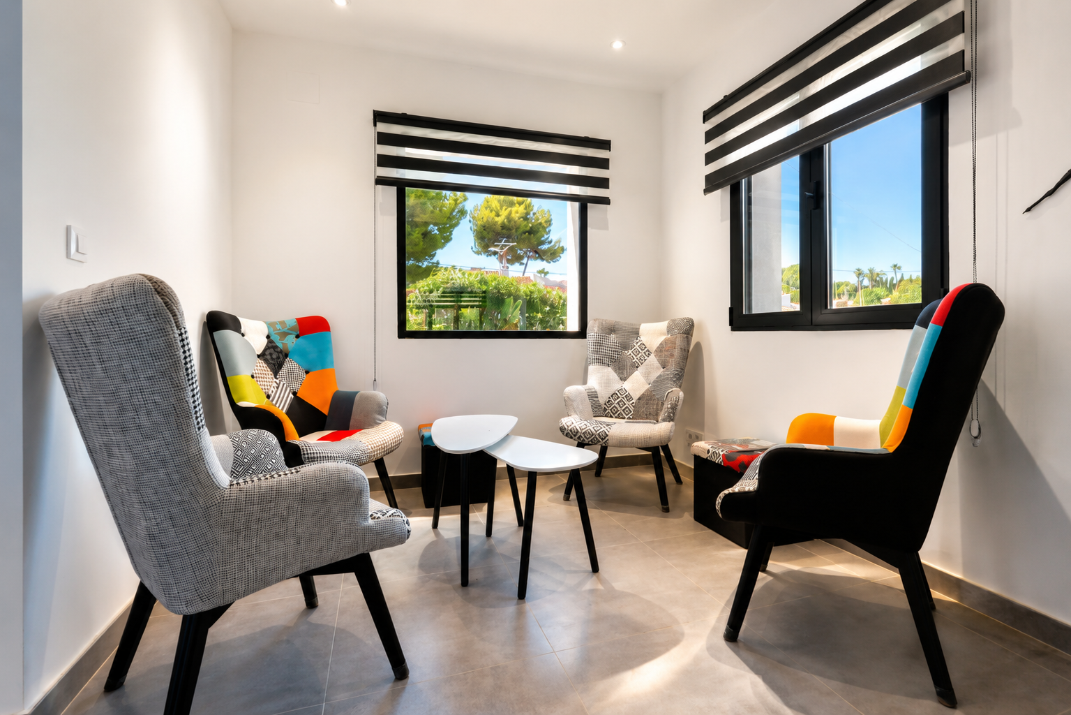Salon lumineux avec fauteuils design et vue sur le jardin à travers des fenêtres à volets.