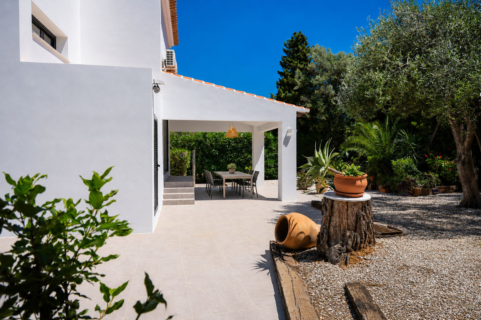 Terrasse couverte avec salle à manger extérieure, entourée d'un jardin méditerranéen et de gravier blanc.