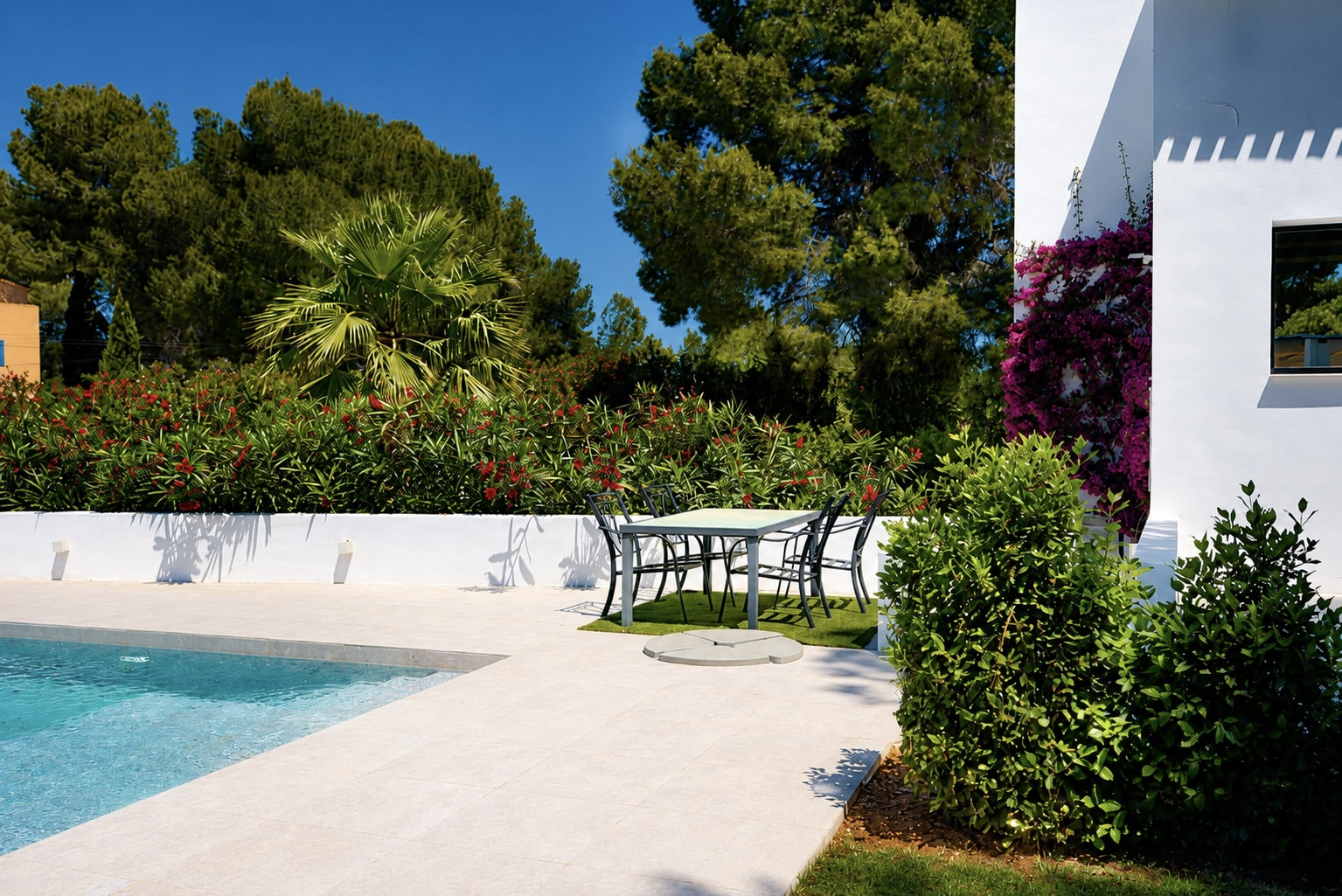 Vue de la piscine avec bordure en pierre claire et coin repas extérieur entouré de verdure.