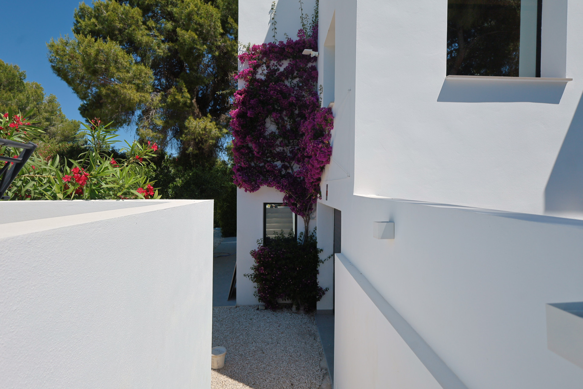 Vue extérieure de la villa, avec des bougainvilliers fleurissant sur la façade blanche et du gravier clair au sol.