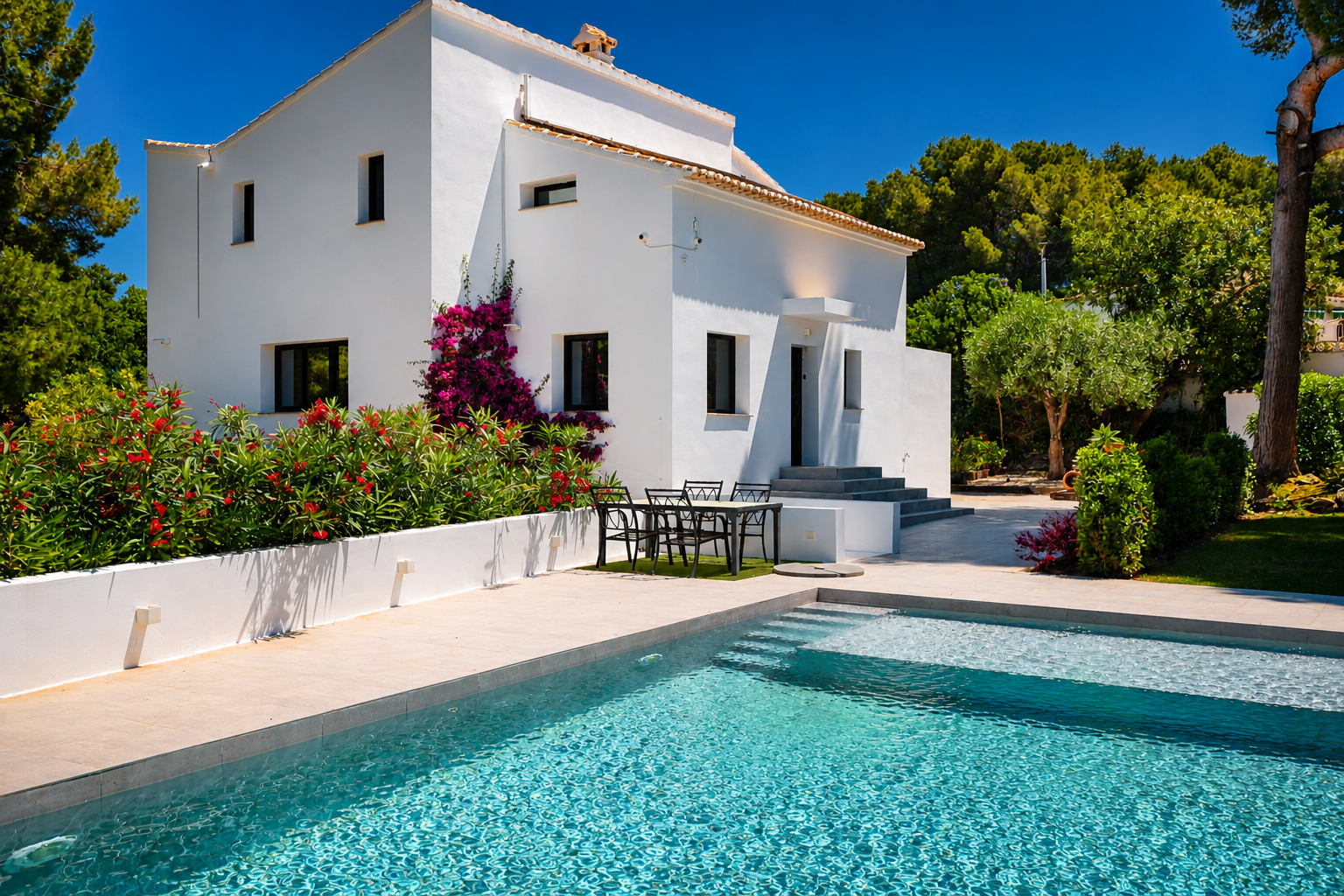 Vue sur la piscine turquoise avec accès par étapes et la façade blanche de la villa ornée de bougainvilliers.