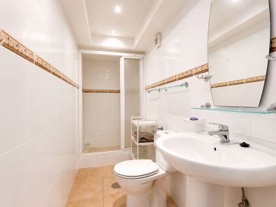 Salle de bain avec carrelage blanc, bordure décorative et sol en céramique couleur terre.