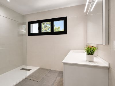 Salle de bain moderne avec douche vitrée, meuble-lavabo blanc et fenêtre à cadre noir apportant de la lumière naturelle.