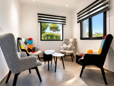 Salon lumineux avec fauteuils design et vue sur le jardin à travers des fenêtres à volets.
