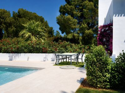Vue de la piscine avec bordure en pierre claire et coin repas extérieur entouré de verdure.