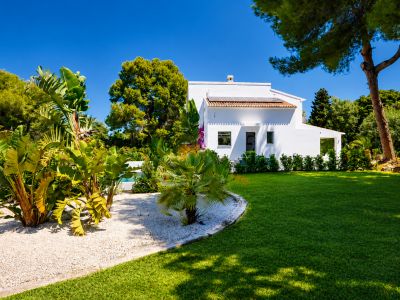 Vue extérieure de la villa avec façade blanche, jardin avec pelouse et végétation tropicale.