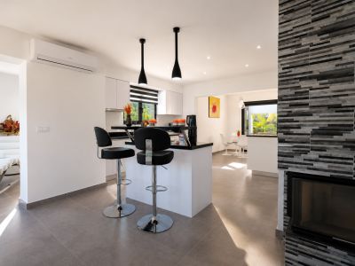 Vue intérieure de la cuisine avec îlot central, tabourets et cheminée revêtue de pierre.
