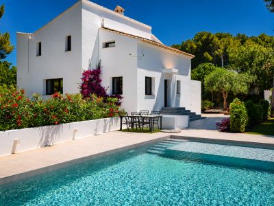 Vue sur la piscine turquoise avec accès par étapes et la façade blanche de la villa ornée de bougainvilliers.