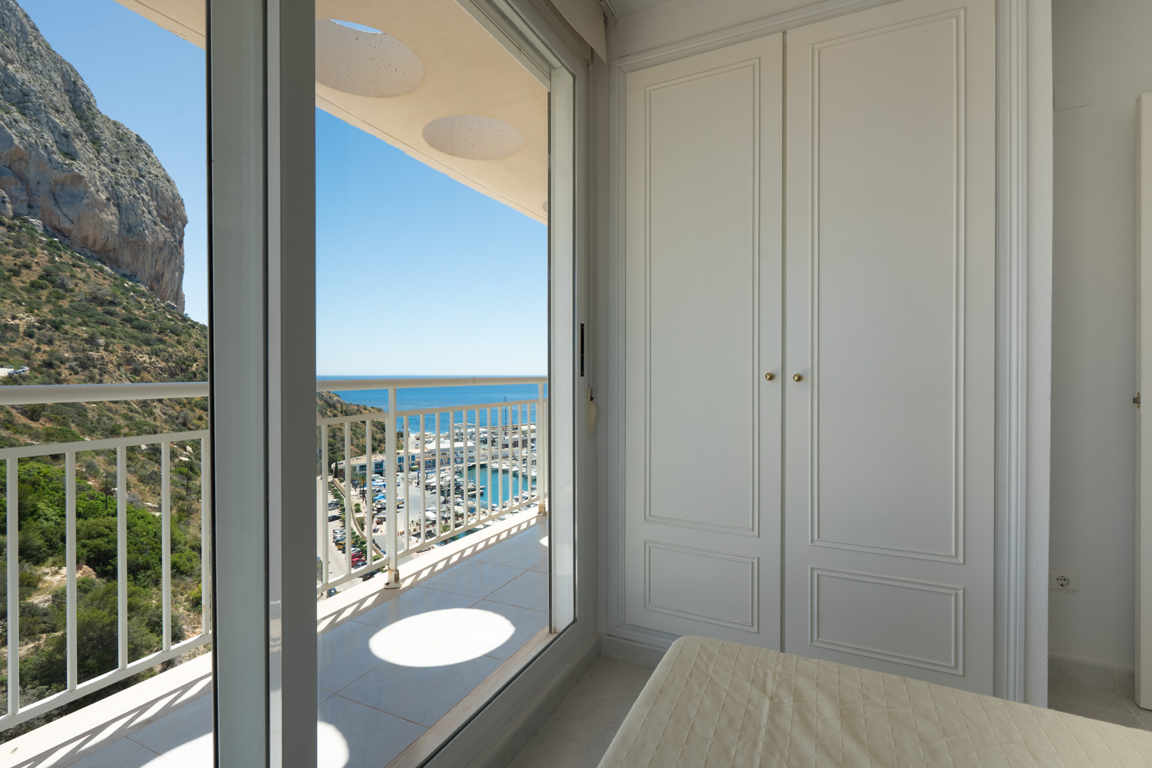 Chambre avec élégant placard intégré blanc et accès direct à un balcon privé. Profitez de vues panoramiques sur le port de plaisance, la mer Méditerranée et l'emblématique Peñón de Ifach.