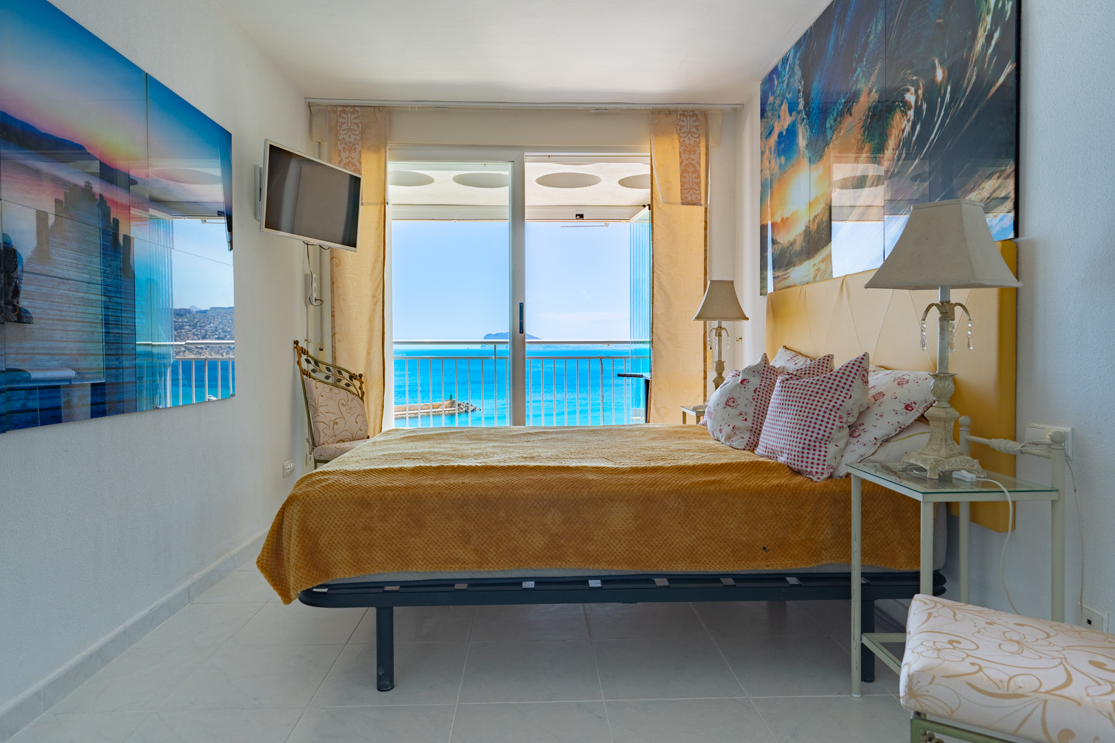 Chambre lumineuse avec tête de lit jaune et accès direct à une terrasse par des portes coulissantes en verre, offrant une vue étendue sur la mer bleue et une terre lointaine.