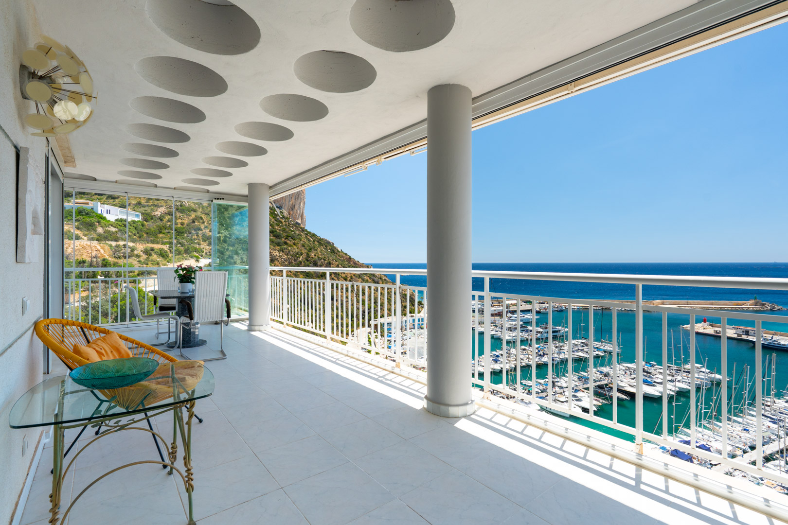 Vaste terrasse couverte avec carrelage clair, plafond à motifs circulaires et vues panoramiques sur le port de Calpe, la mer Méditerranée et le Peñón de Ifach.