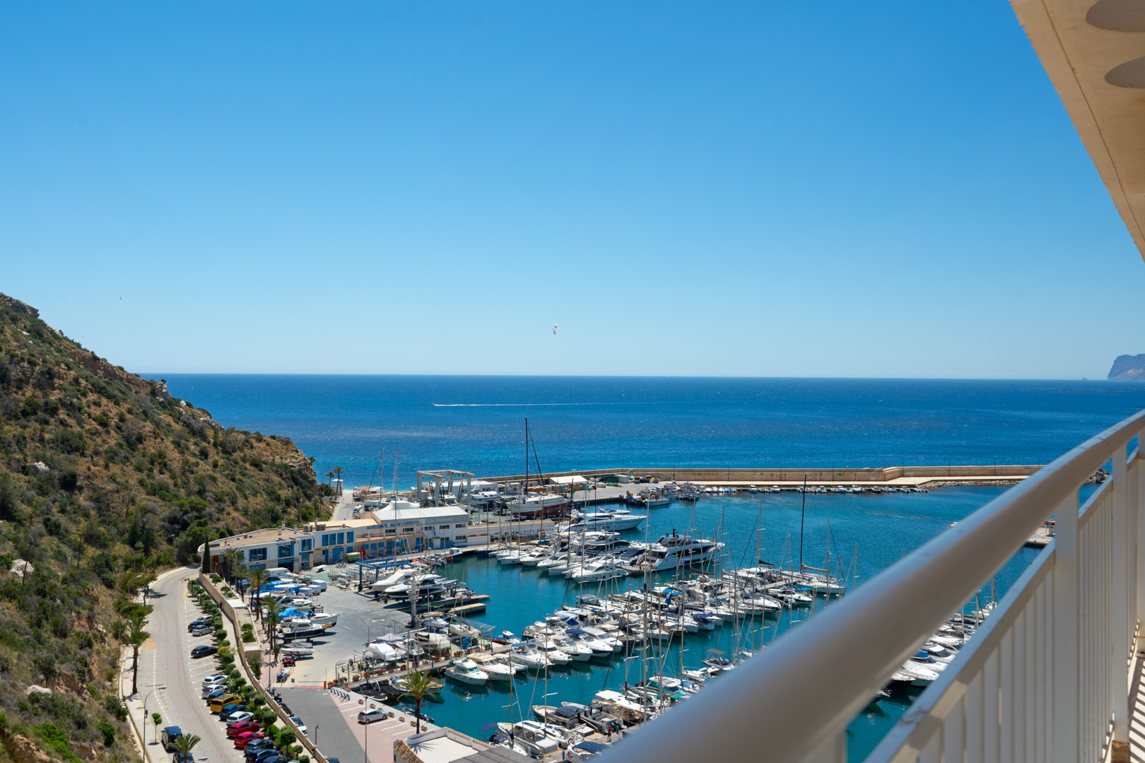 Vue panoramique depuis le balcon, présentant le port de plaisance animé de Calpe rempli de yachts, la vaste mer Méditerranée et la colline verdoyante.