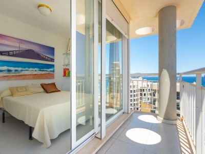 Chambre lumineuse avec accès direct à un balcon privé, dotée de portes coulissantes en verre, de balustrades blanches et de vues sur la mer.