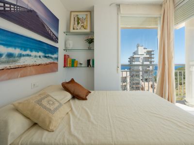 Chambre lumineuse avec un lit confortable, décor mural artistique, étagères en verre et accès direct à un balcon avec vue mer et ville.