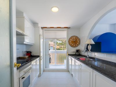 Cuisine semi-ouverte avec meubles blancs, plans de travail en granit foncé et fenêtre offrant une vue sur la colline. Espace buanderie intégré.