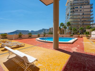 Espace piscine commun avec pavé texturé rouge et jaune, offrant des vues lointaines sur la mer et les montagnes.