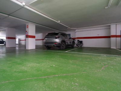 Place de parking privée dans un garage souterrain éclairé, avec sol en résine verte, piliers blancs à rayures rouges et extincteur. Un SUV gris est garé à côté d'un vélo.