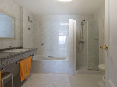 Salle de bain principale avec carrelage mural effet marbre, plan vasque en granit, baignoire et cabine de douche vitrée séparée.