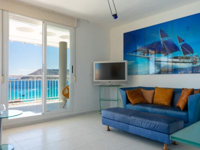 Salon lumineux avec canapé bleu, œuvre d'art marine et portes coulissantes s'ouvrant sur une terrasse offrant une vue panoramique sur la mer.