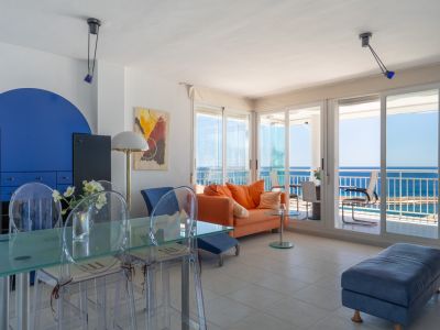 Salon-salle à manger lumineux avec canapé orange, table en verre et accès direct à une terrasse vitrée offrant des vues panoramiques sur la mer.