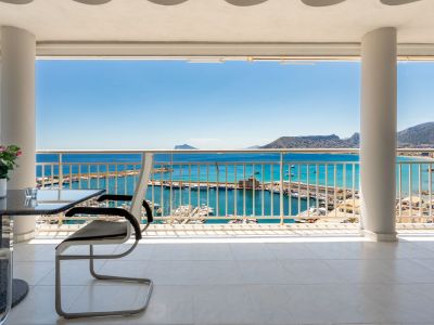 Terrasse couverte avec carrelage blanc et colonnes structurelles, offrant une vue panoramique directe sur le port de plaisance de Calpe, la mer Méditerranée et les montagnes lointaines.