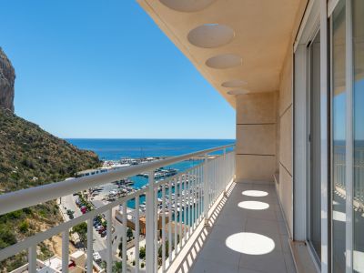 Vaste balcon offrant une vue directe sur la marina de Calpe, la mer Méditerranée et l'emblématique Peñón de Ifach, avec carrelage et portes coulissantes en verre.