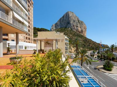 Vue sur l'emblématique Peñón de Ifach et la route côtière, encadrée par des palmiers et de la verdure au premier plan, depuis la terrasse du complexe.