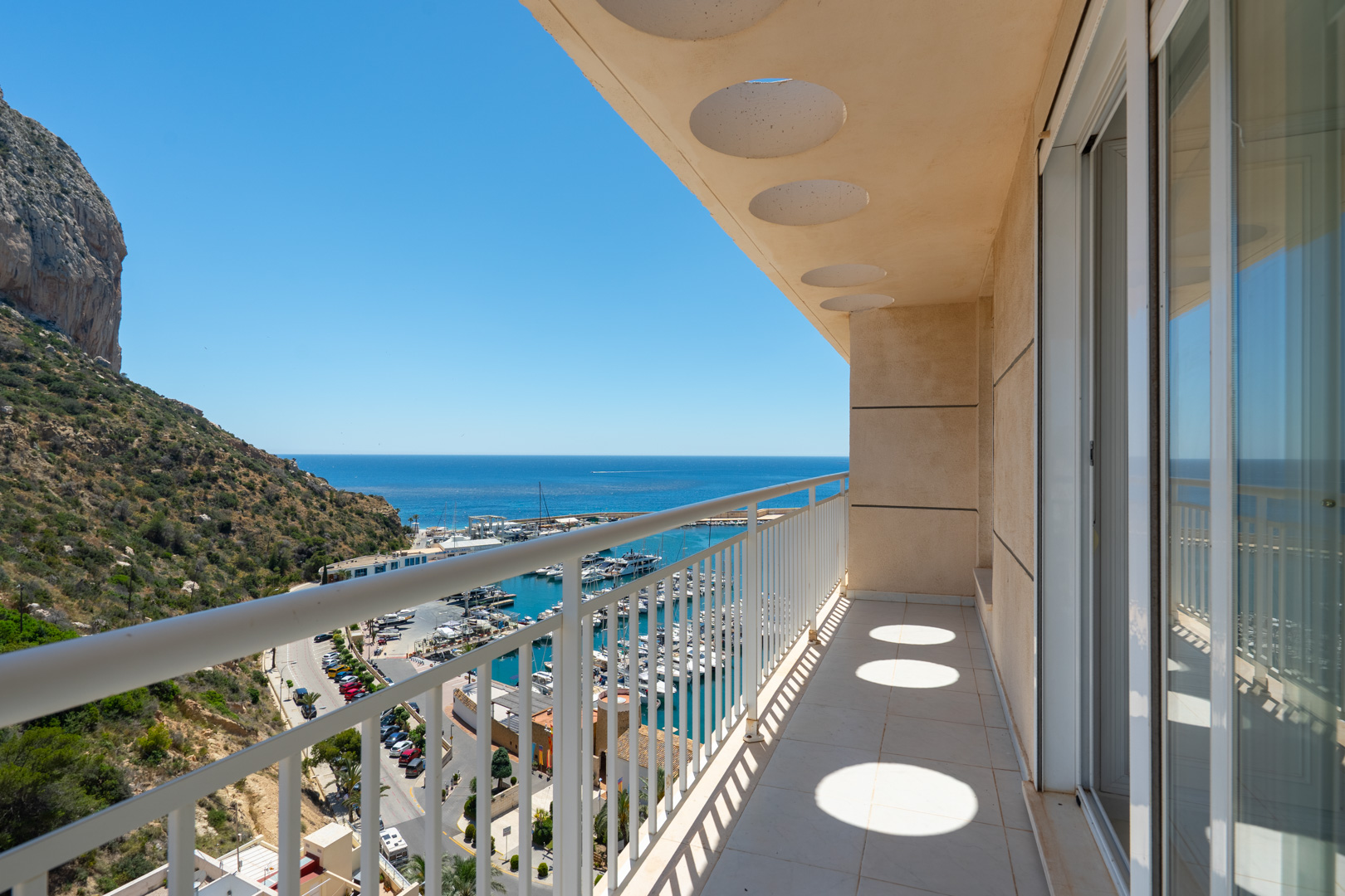 Grande terrasse privée avec sol carrelé et balustrade blanche, dotée d'un plafond aux motifs circulaires. Vues directes sur le port de plaisance, la mer et le Peñón de Ifach.