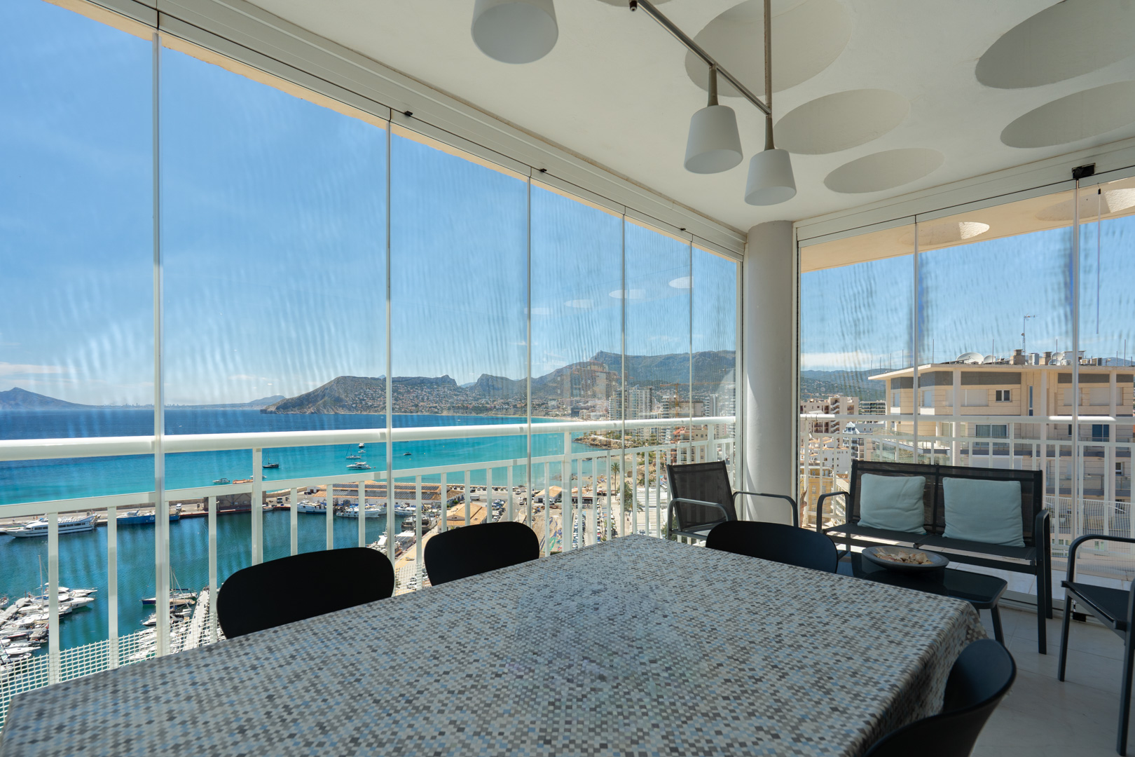 Terrasse vitrée avec espace repas, offrant des vues directes sur le port de Calpe, la mer turquoise et l'emblématique Peñón de Ifach.