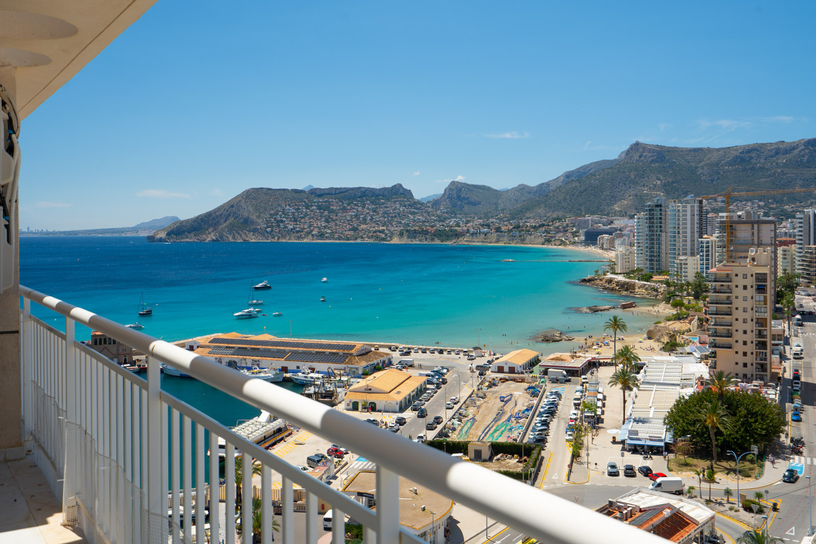 Vue en hauteur depuis la terrasse sur le port animé de Calpe, la baie turquoise et le paysage montagneux de la Costa Blanca sous un ciel clair.