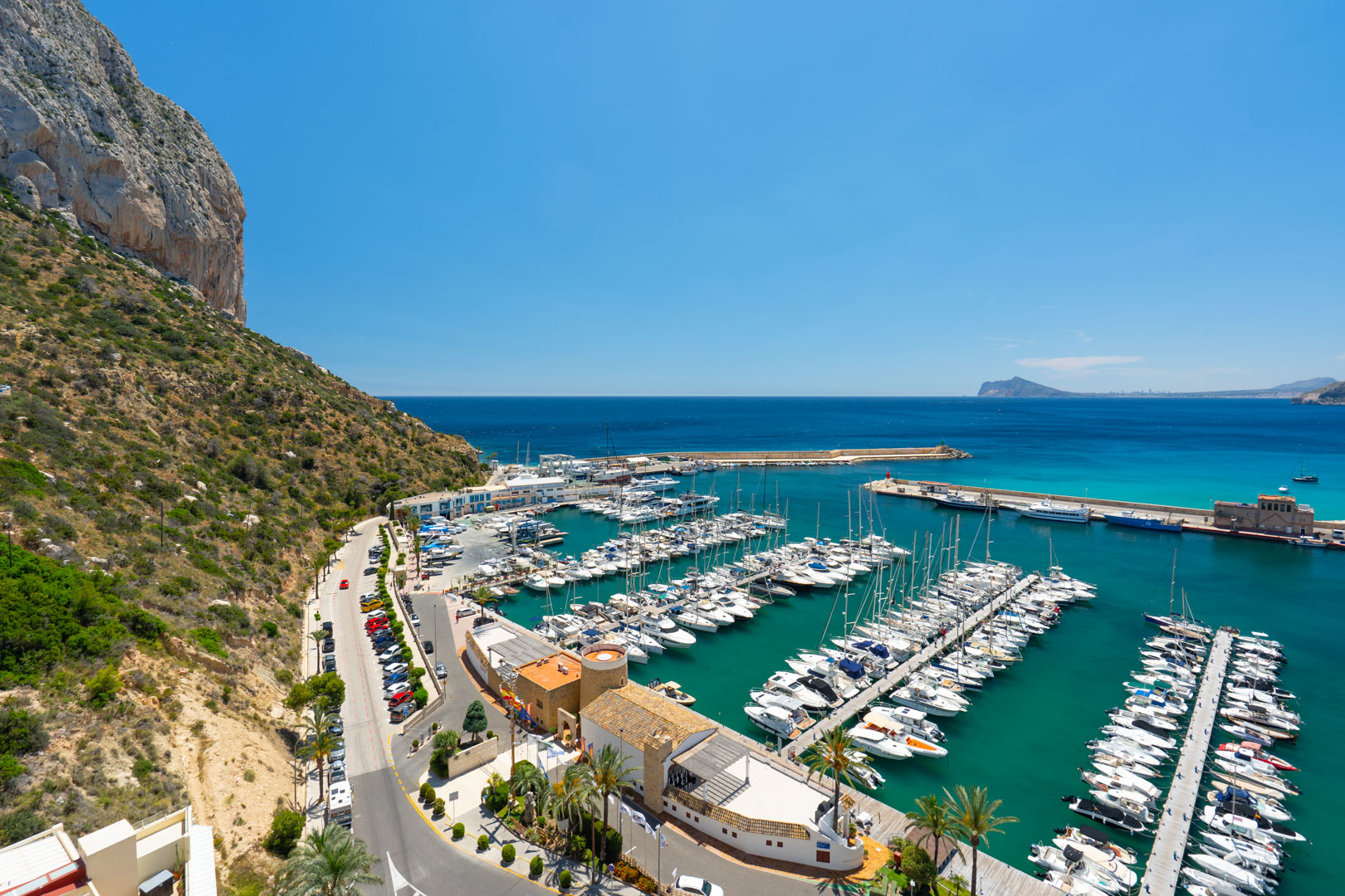 Vue panoramique du port de plaisance animé de Calpe, encadré par le majestueux Peñón de Ifach et les eaux turquoise claires de la Méditerranée.