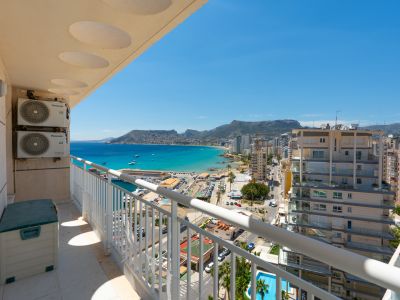 Balcon offrant une vue panoramique sur le port de Calpe, la baie turquoise et le littoral urbain, encadré par une balustrade blanche et des unités de climatisation extérieures.