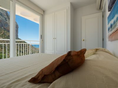 Chambre avec accès direct au balcon, offrant des vues sur l'emblématique Peñón de Ifach, la colline verdoyante et la mer Méditerranée. Armoire encastrée blanche.