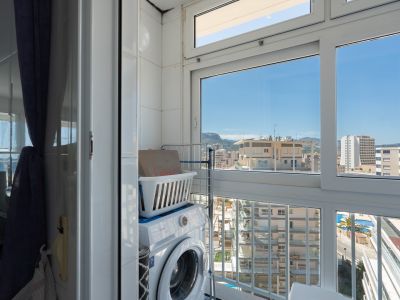 Coin buanderie pratique avec machine à laver et étagère, intégré dans un espace carrelé avec de grandes fenêtres offrant des vues urbaines sur les bâtiments, les montagnes et une piscine.