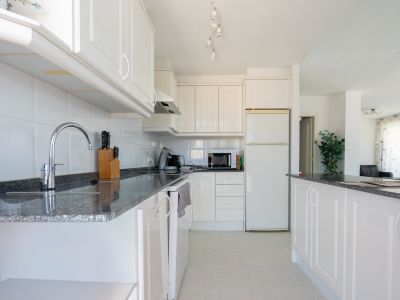 Cuisine fonctionnelle avec des armoires blanches, des plans de travail en granit foncé et un carrelage mural blanc. Équipée d'appareils essentiels et d'un bar ouvrant sur le salon.