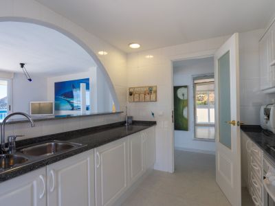 Cuisine fonctionnelle avec des plans de travail foncés et un double évier, reliée par une arche à un salon offrant des vues sur la mer et le Peñón de Ifach.