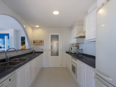 Cuisine fonctionnelle avec meubles blancs, plans de travail en granit foncé et appareils intégrés, reliée au salon par une arche.