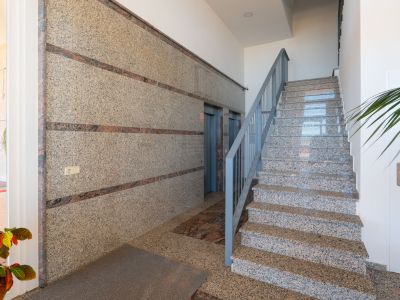 Espace commun de l'immeuble avec murs en granit poli à bandes décoratives foncées, escalier en granit assorti avec rampe grise et deux ascenseurs, sous éclairage encastré.