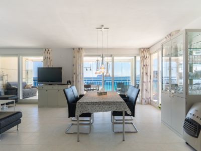 Grand espace de vie et salle à manger ouvert avec carrelage clair, comprenant une table moderne et des vues directes sur la mer par de larges baies vitrées menant à une terrasse vitrée.