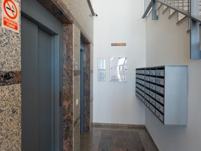 Hall d'entrée avec deux portes d'ascenseur encadrées de granit moucheté, un tapis de sol en granit foncé contrastant et une cage d'escalier métallique.